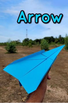 a hand holding a blue paper airplane with the word arrow above it and an image of trees in the background