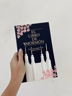 a person holding up a book in front of a white wall with pink flowers on it