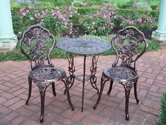 an outdoor table and two chairs on a brick patio with pink flowers in the background