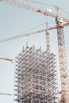 two cranes are standing next to a building under construction with scaffolding on it