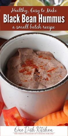 a white bowl filled with black bean hummus next to sliced carrots