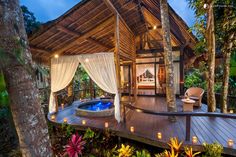 a wooden deck with a hot tub surrounded by greenery and candles in the evening