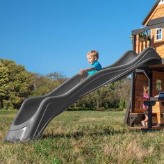 a little boy is playing on a slide in the yard with his house behind him