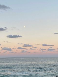 the moon is setting over the ocean with rocks in front of it and clouds in the sky