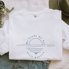 "Wear your faith close to your heart! This white Comfort Colors sweatshirt features a minimalistic ocean sunset (or sunrise!) drawing with the verse Psalm 23:2 in reference: \"he leads me by still waters.\" With A Wildflower aims to blend faith and fashion, focusing on minimalist and boho styles. Comfort Colors sweatshirts are super soft and super comfy, featuring garment-dyed 80% ring-spun cotton and 20% polyester. Each sweatshirt comes with a relaxed unisex fit, a rolled-forward shoulder, and Psalm 23 Shirt, Christian Tshirts Designs Woman, Christian Sweatshirt Designs, Sunrise Drawing, Christian Sweaters, Clothes Embroidery, Clothes Embroidery Diy, Personalized Bible, Christian Tshirt