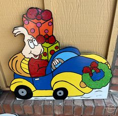 a wooden sign depicting a cartoon character driving a car with presents on it's roof