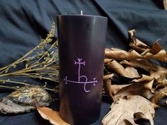 a purple candle sitting on top of a table next to dry leaves