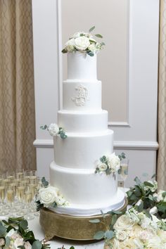 a wedding cake with white flowers and greenery on the table next to champagne glasses