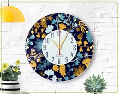 a wall clock with blue and yellow floral designs on it next to a potted plant