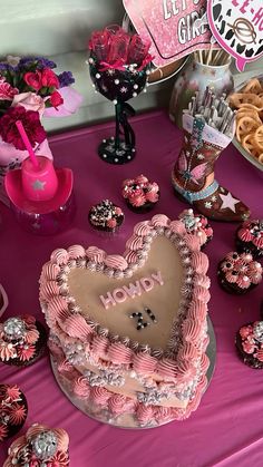 a heart shaped cake sitting on top of a table next to cupcakes and cookies