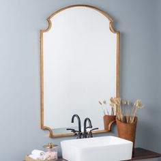 a bathroom sink sitting under a mirror next to a wooden shelf with flowers on it