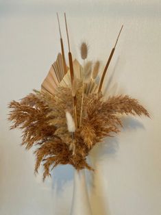 a vase filled with dry grass and feathers on top of a table next to a wall