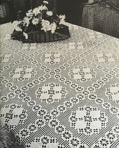 a table topped with a basket of flowers on top of a table covered in white crocheted doily