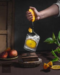 a person pouring orange juice into a glass with slices of fruit on the table next to it