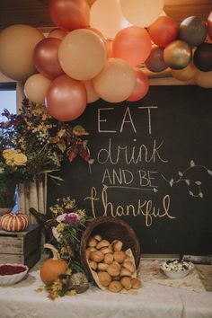 a table topped with lots of balloons next to a chalkboard sign that says eat drink and be grateful