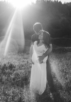 black and white photograph of a couple kissing in a field with the sun behind them