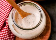 a wooden spoon in a jar filled with ranch dressing on top of a red and white checkered cloth