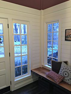 a room with two windows and a bench in front of the door to another room