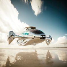 a futuristic car flying through the air on top of a sandy beach with clouds in the background