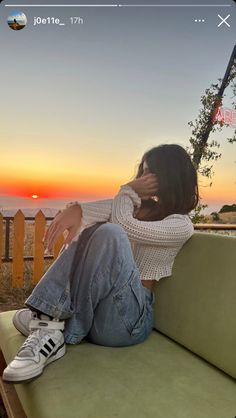 a woman sitting on top of a green couch next to the ocean at sun set