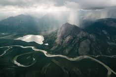 an aerial view of mountains and rivers under a cloudy sky with sun rays coming through the clouds