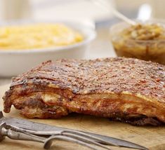 a piece of meat sitting on top of a cutting board next to a fork and knife