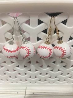 three baseball earrings hanging from hooks in a basket