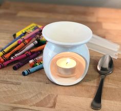 a white candle holder sitting on top of a wooden table next to crayons