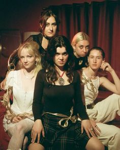 a group of women sitting next to each other in front of a red curtained wall