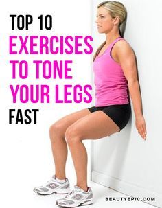 a woman in pink shirt and black shorts leaning against wall with her leg up on the wall