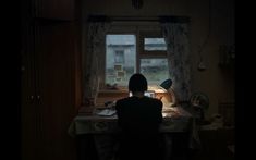 a person sitting at a desk in front of a window with a lamp on it