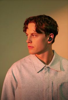 a young man with ear buds on his ears looking off to the side while standing in front of a wall