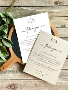 the wedding stationery is laid out on top of a wooden platter with greenery