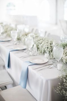 the table is set with white and blue linens, baby's breath flowers, and silverware