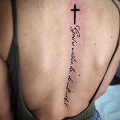 a cross tattoo on the back of a woman's upper body, with words written in cursive writing