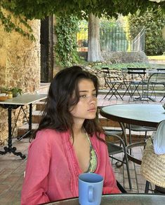 a woman sitting at an outdoor table with a blue coffee cup in front of her