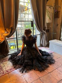 a woman in a black dress sitting on the floor next to a window with curtains