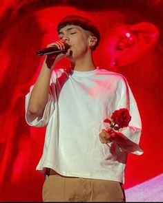 a young man singing into a microphone while holding a red rose in his right hand