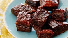 a blue plate topped with cubes of meat on top of a wooden table next to a yellow napkin