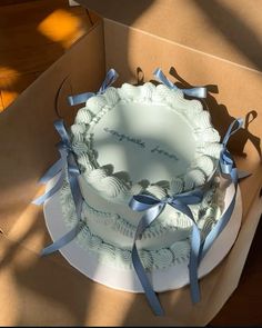 a white cake with blue ribbons in a box