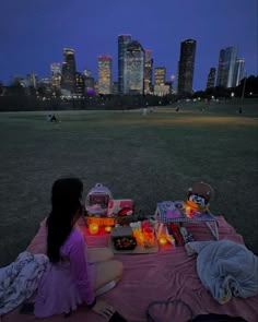 a woman sitting on top of a pink blanket in front of a cityscape