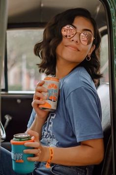 a woman sitting in the back seat of a car holding a can and wearing glasses