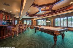 a pool table in the middle of a living room with chairs and tables around it