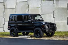 a black mercedes g - class is parked in front of a wall