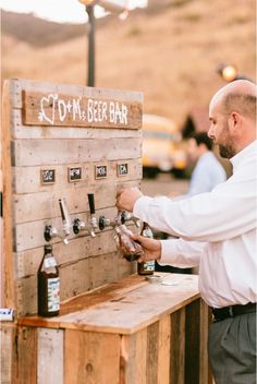 a man standing next to a wooden table filled with beer bottles and tappers on top of it