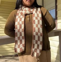 a woman standing in front of a house with her hands on her hips wearing a scarf