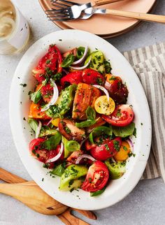 a salad with tomatoes, onions and other vegetables on a plate next to utensils