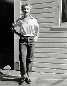 an old photo of a woman standing in front of a house with her hands on her hips