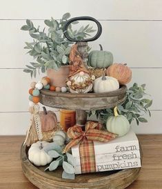 a three tiered tray with pumpkins and other fall decorations on it, sitting on a wooden table