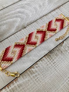 a red and white beaded bracelet sitting on top of a wooden table next to a pair of scissors